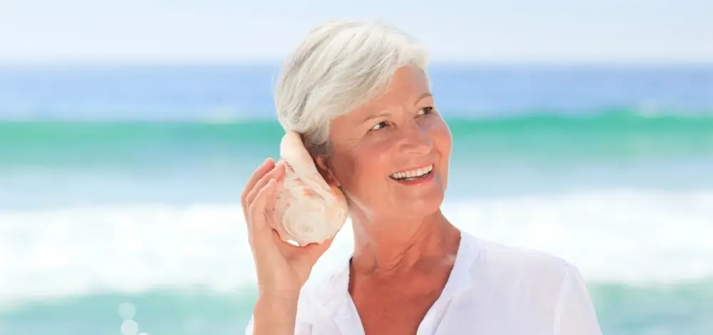 Happy senior woman listening to seashell at beach